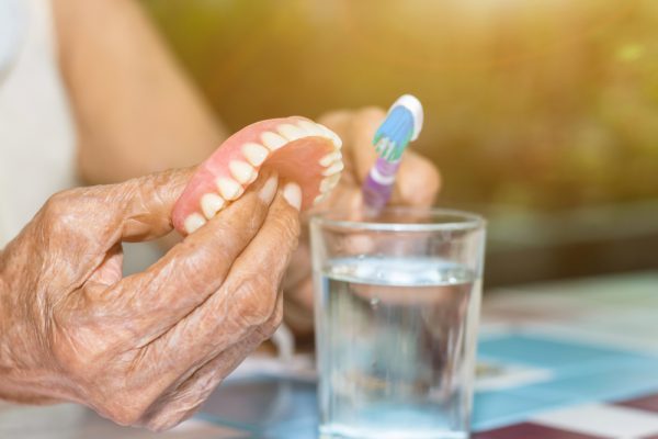 person cleaning dentures with toothbrush