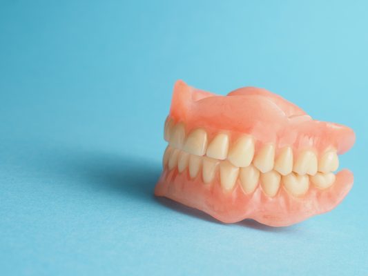 Complete dentures model showcasing artificial teeth and acrylic base against a blue background, illustrating the restoration of smile and oral function for individuals with tooth loss.